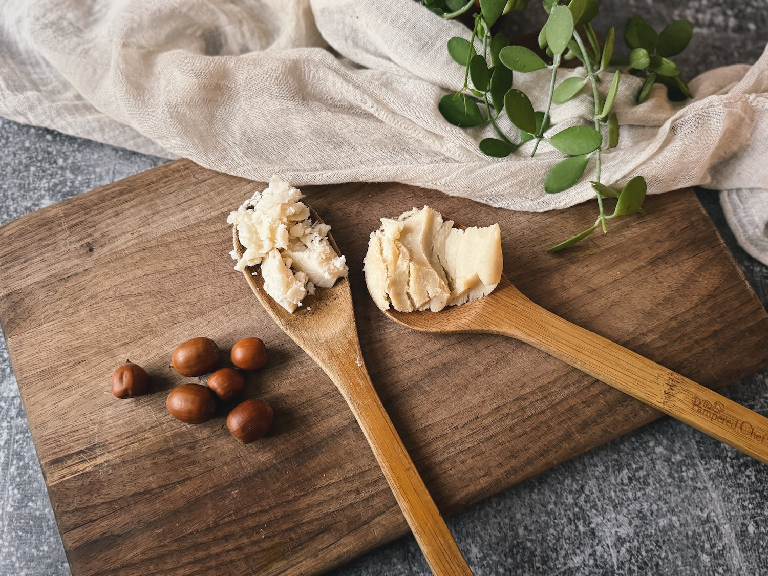 Wooden spoons with tallow and lard on a rustic board beside acorns and greenery, representing the natural ingredients used in traditional skincare.