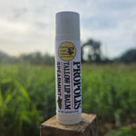 Greene Grass Tallow Spearmint Propolis Tallow Lip Balm, 0.15 oz tube on a wooden post with a green field in the background.