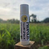 Greene Grass Tallow Spearmint Propolis Tallow Lip Balm, 0.15 oz tube on a wooden post with a green field in the background.