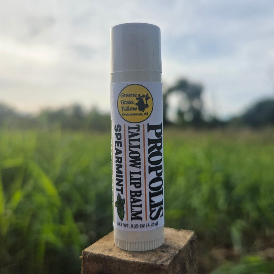 Greene Grass Tallow Spearmint Propolis Tallow Lip Balm, 0.15 oz tube on a wooden post with a green field in the background.